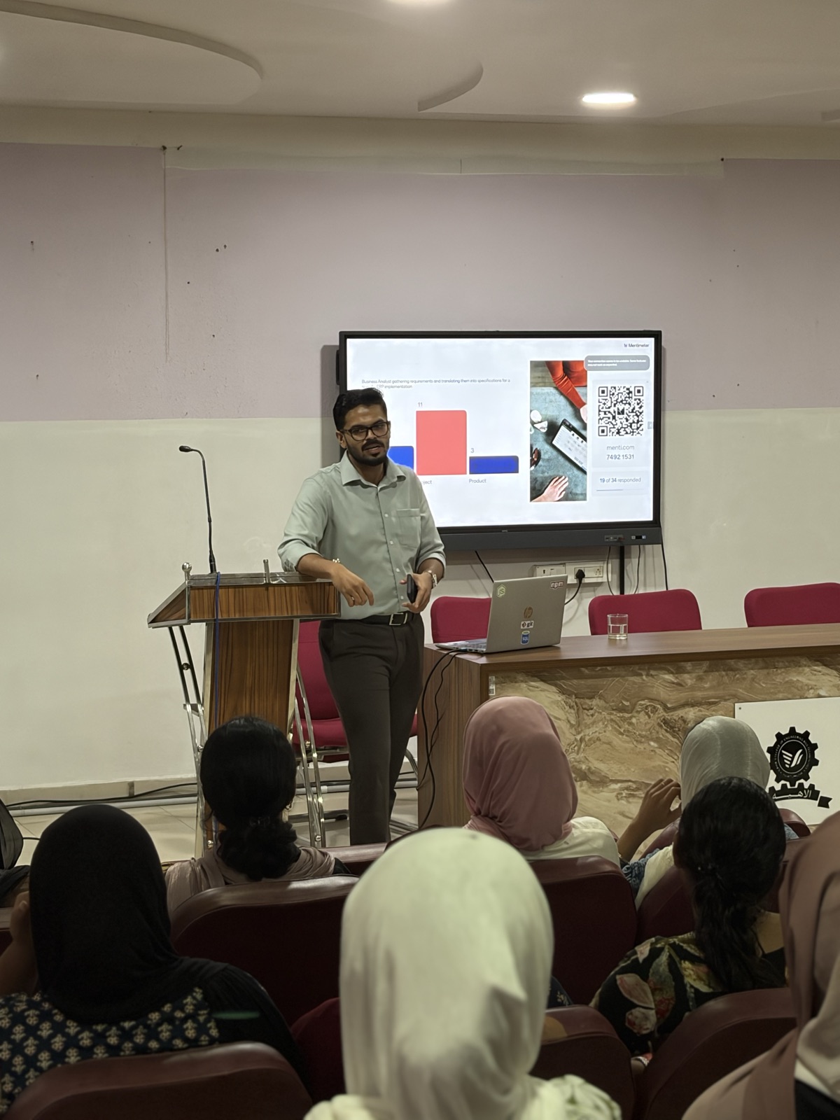 Ameen Abdulsalam presenting a slide to a seated audience in a lecture hall.